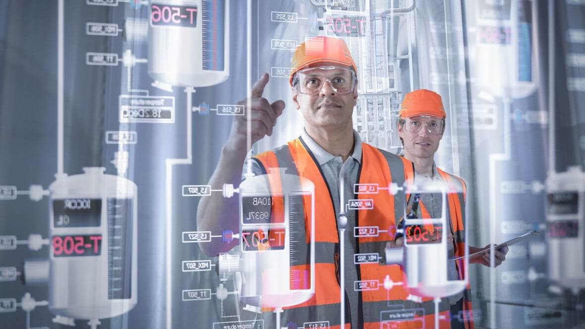 Two workers in orange vests and helmets looking at screen.